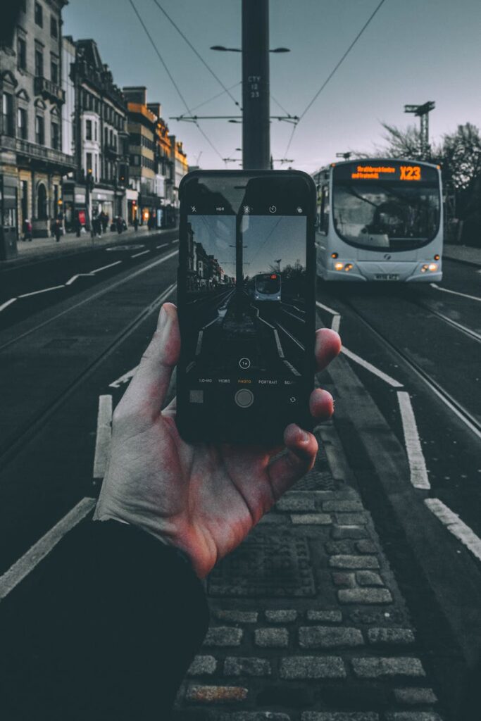 Hand holding a smartphone capturing a city street with a bus at twilight.