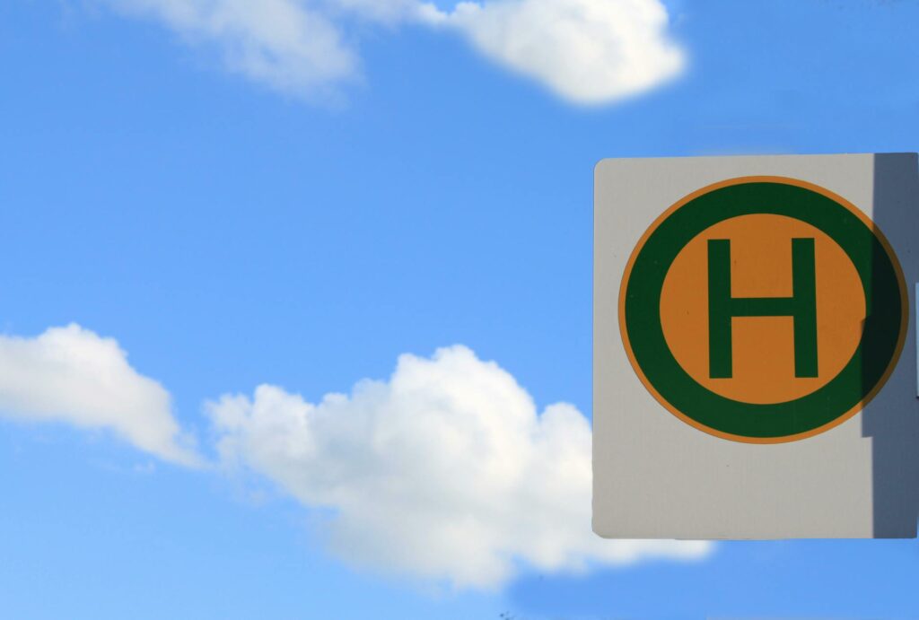 Street sign with the letter 'H' against a bright blue sky with clouds.