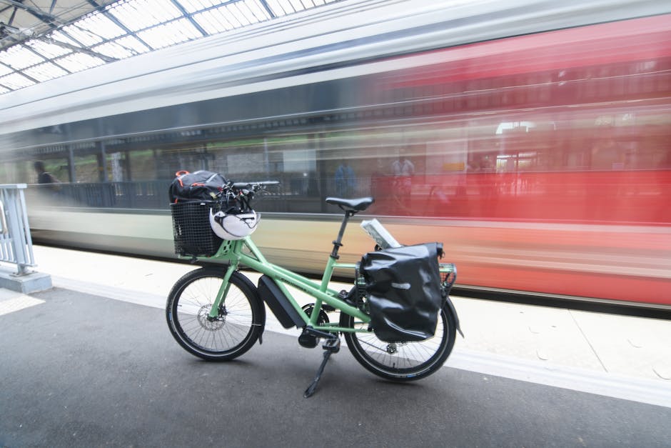 A green cargo bike parked at a train station platform in France, with a train motion blur in the background.